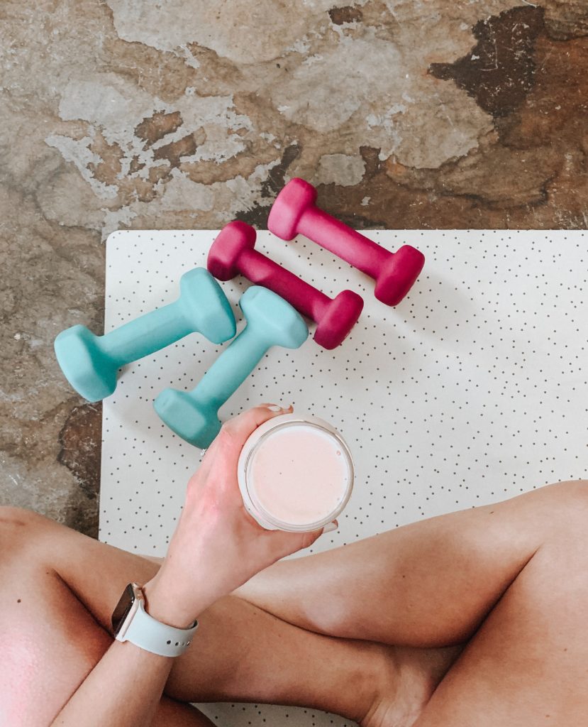 A girl holding a smoothie in front of some dumbbells
