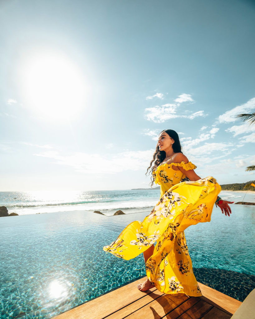 Isabella on a pier next to an infinity pool wearing a yellow dress