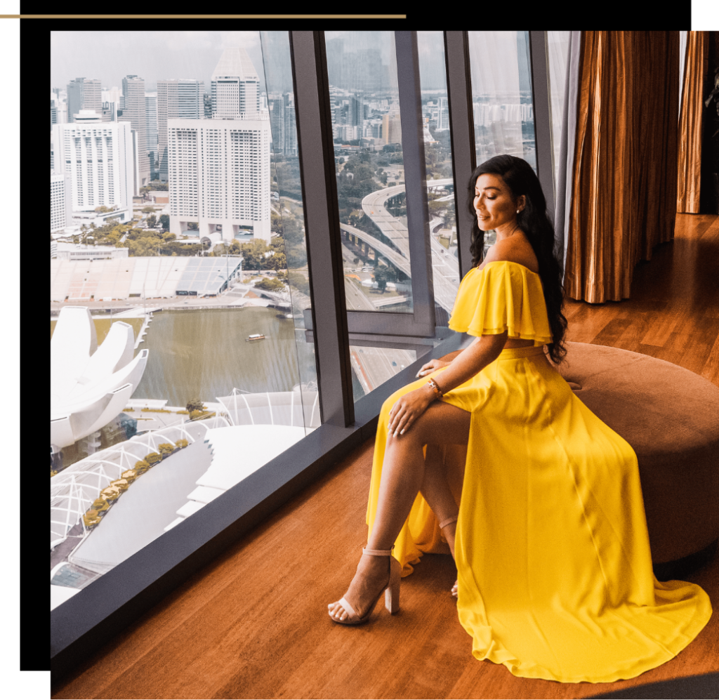 Isabella sitting inside the luxury Marina Bay Sands hotel in Singapore overlooking the city in an orange dress