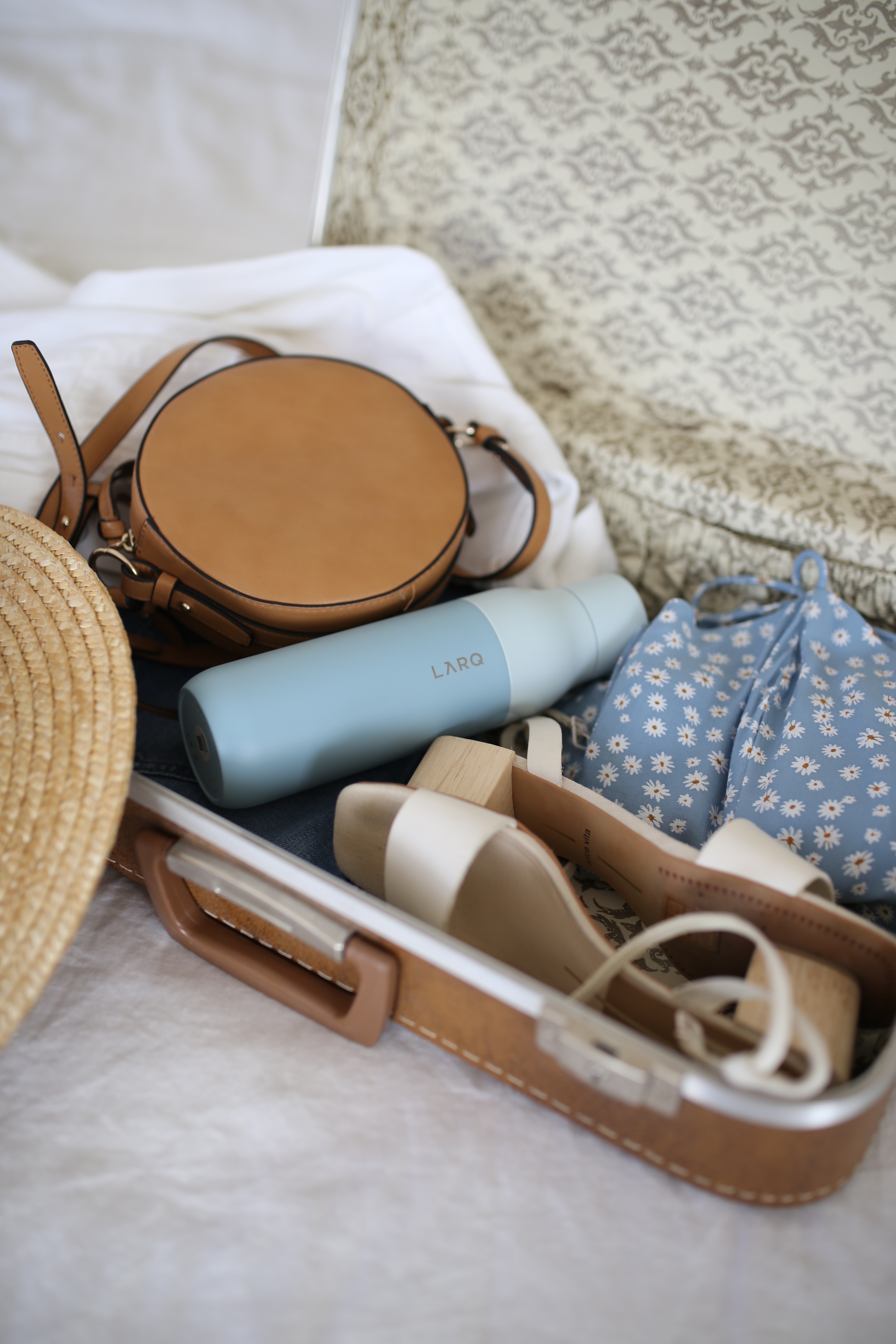 A mini suitcase open with shoes, a handbag and a hat