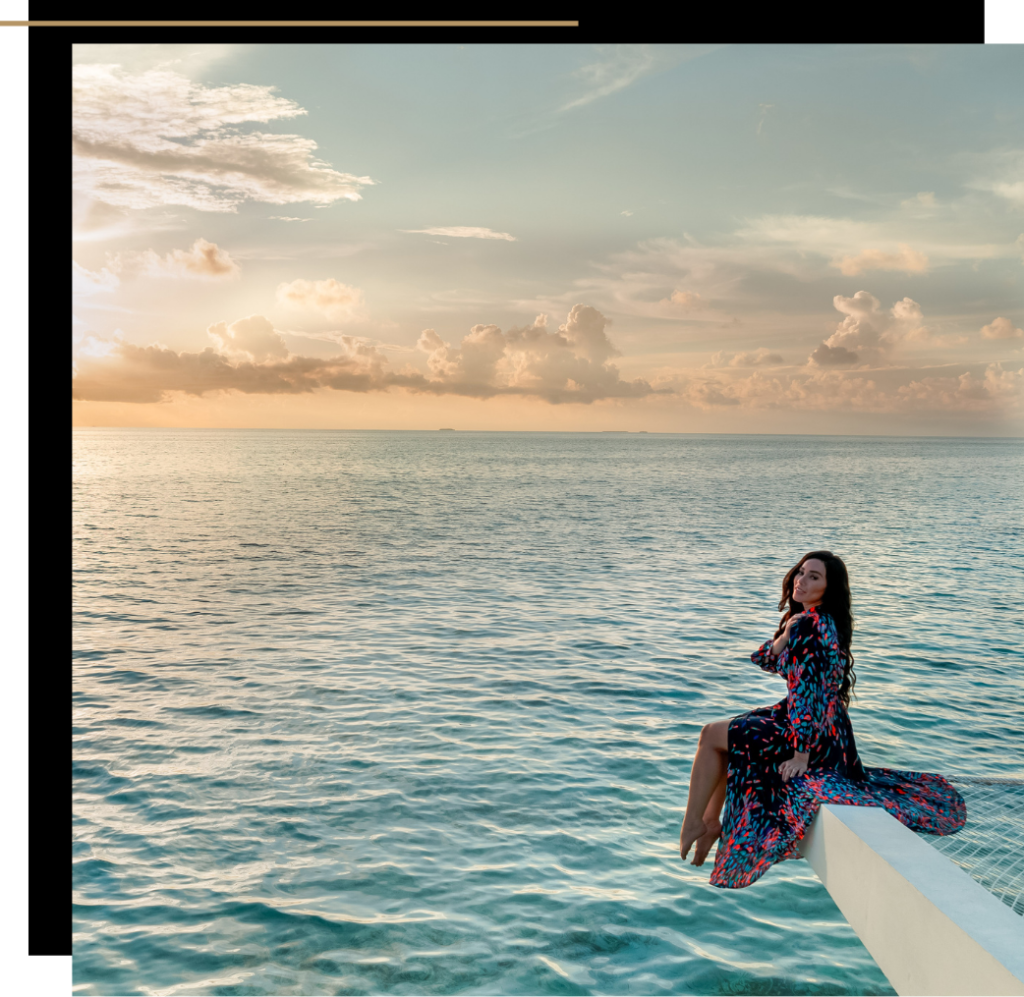 Isabella sitting on a beam over the ocean at sunset in The Maldives